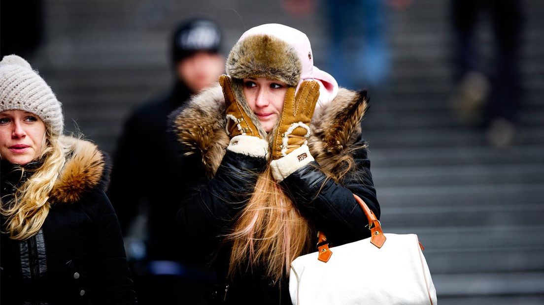 Een vrouw trotseert de kou met een muts op en handschoenen aan