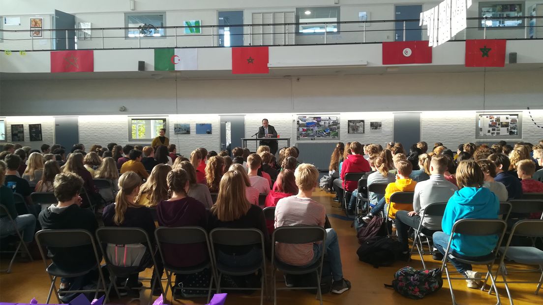 De ambassadeur spreekt in de versierde hal de leerlingen toe.