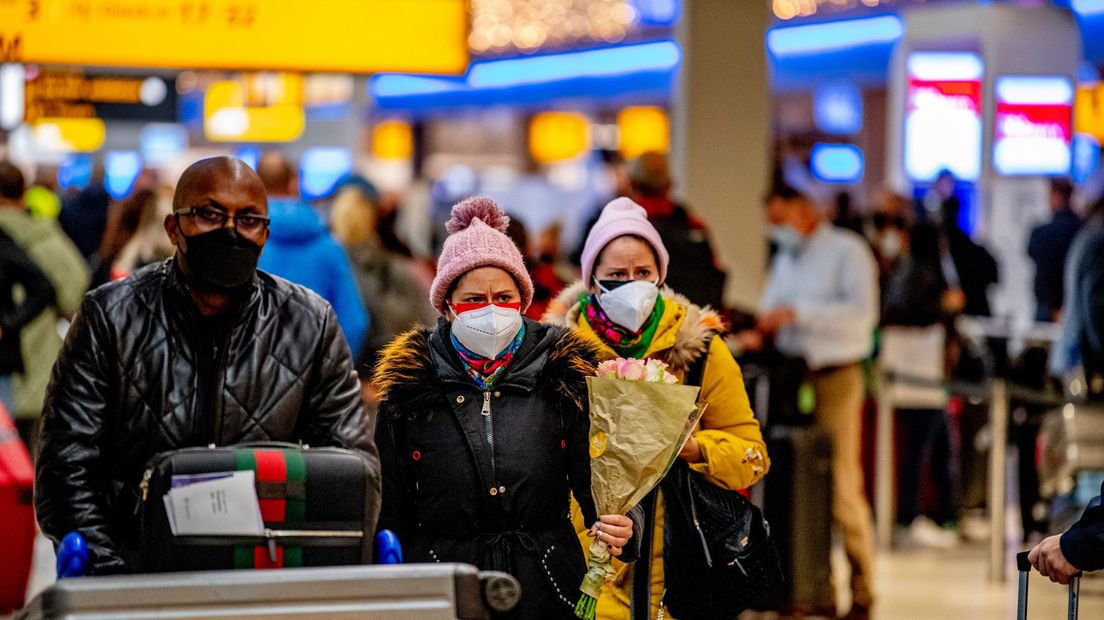 Op Schiphol staan reizigers met mondkapjes in lange rijen.