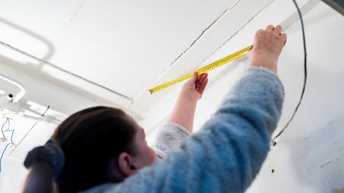 Een vrouw meet de grootte van een scheur in haar huis op