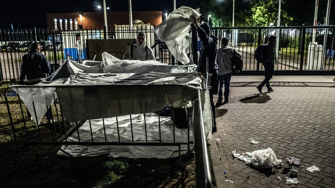 Asielzoekers maken een slaapplaats van dranghekken en dekens buiten voor de poort bij het aanmeldcentrum