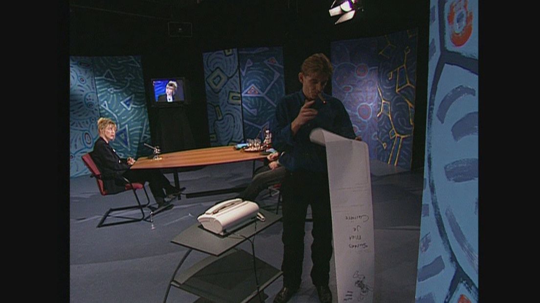 Beeld uit 'De Hunnen'. Jan Kikkert, met sigaar, leest de faxen terwijl Jan Medendorp Johanna ter Steege interviewt.