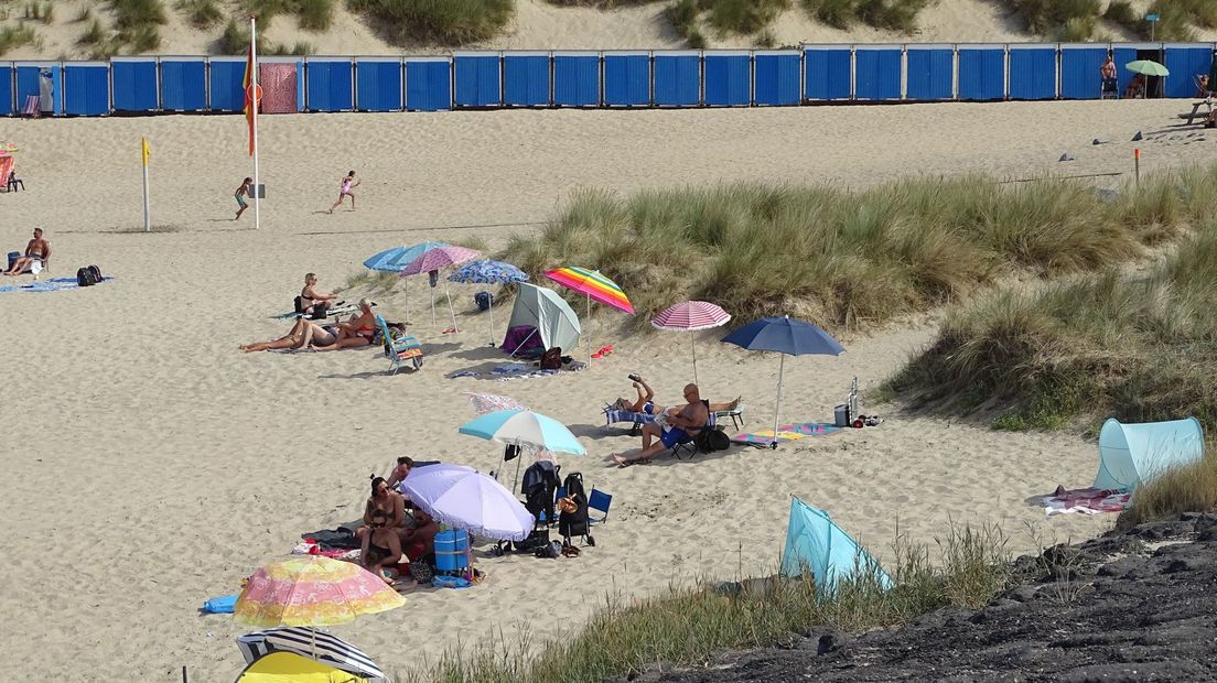 Strandgangers zoeken beschutting tegen de zon onder parasols op Nollestrand bij Vlissingen