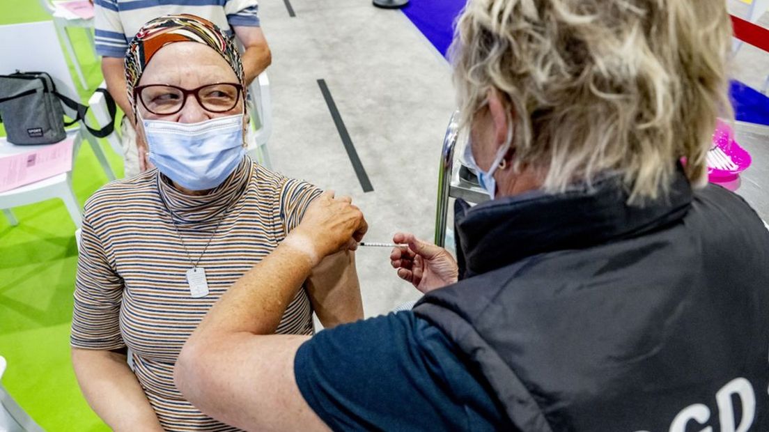 Mensen laten zich vaccineren door GGD-personeel.