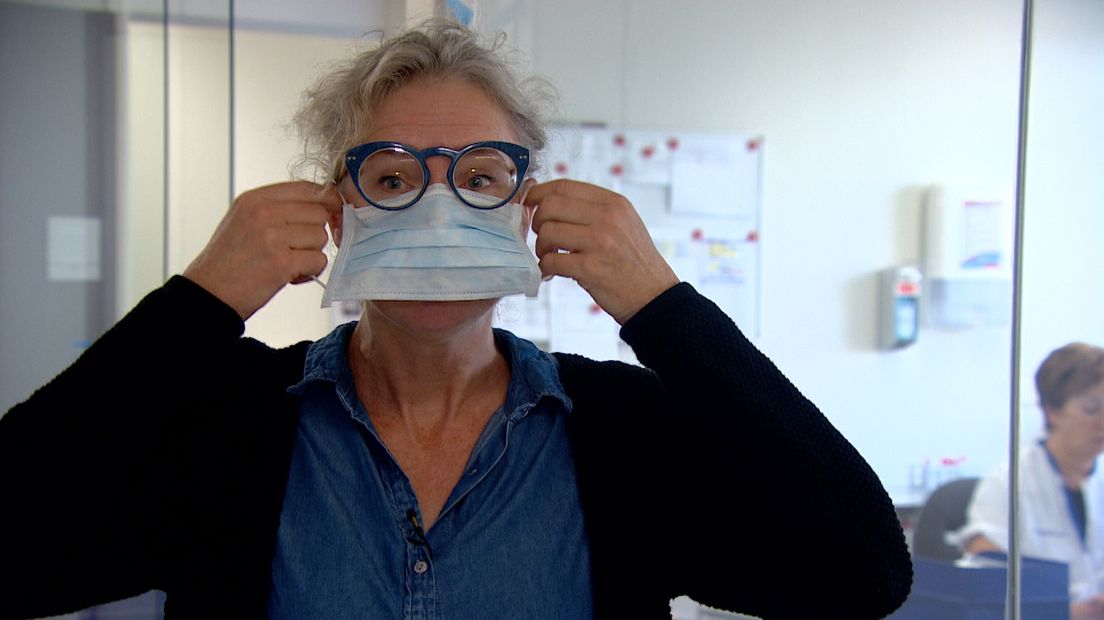 Ina Willemsen demonstreert hoe je een mondkapje opdoet.