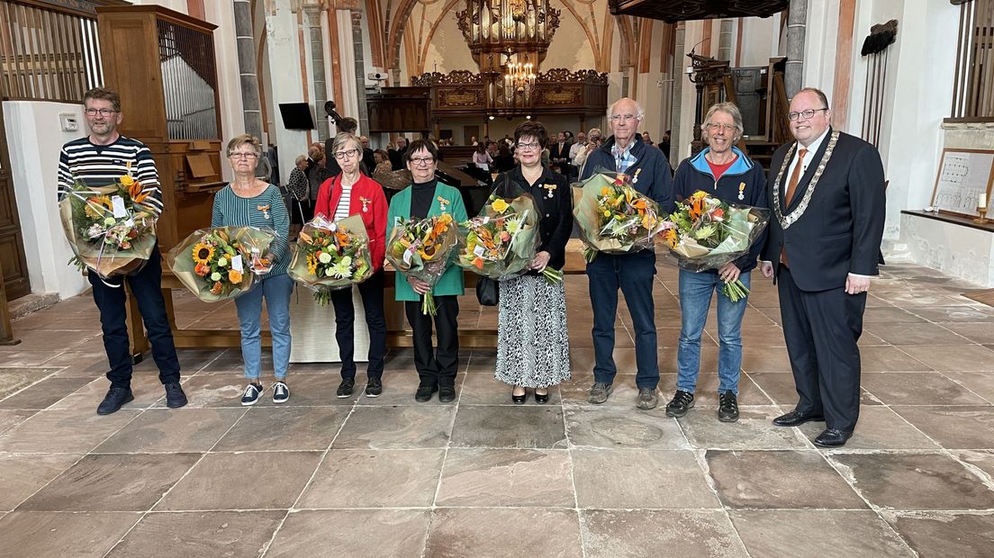 De zeven inwoners van de Eemsdelta die een lintje kregen en burgemeester Ben Visser in de Nicolaïkerk