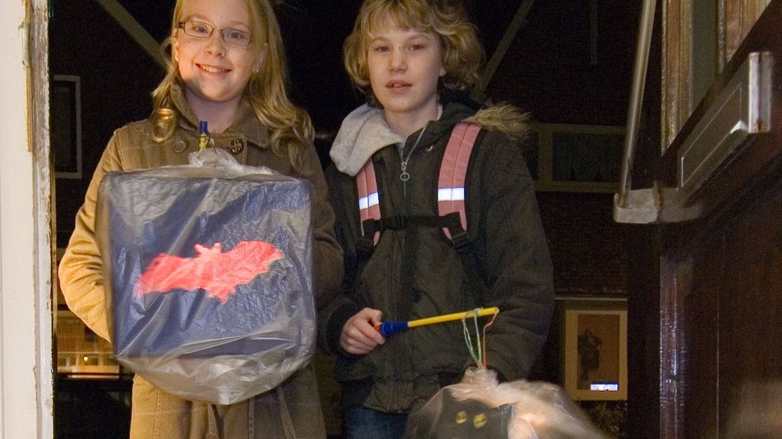 Twee meisjes met lampionnen die zijn ingepakt in een plastic zak vanwege de regen