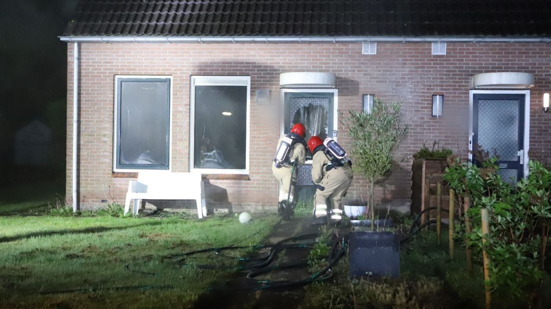 De brandweer forceert de voordeur bij de woning in Nieuw-Buinen