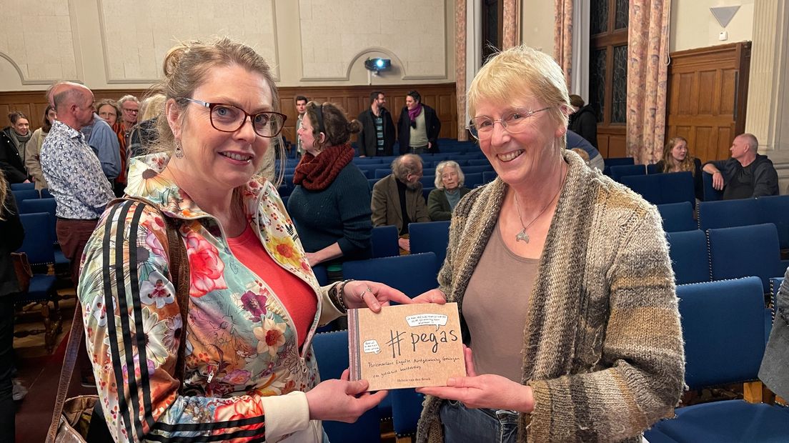 Van den Broek overhandigt het boekje aan gedupeerde Bea Blokhuis (rechts)