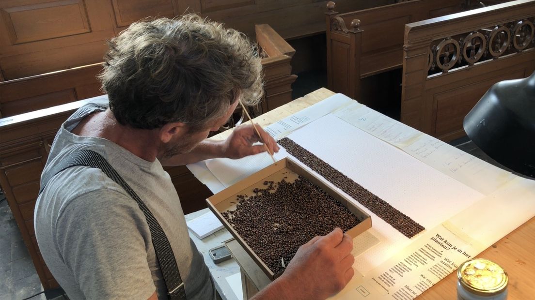 Marc de Groot is in de kerk van Saaxumhuizen bezig met een kunstwerk van duizenden zaadjes.