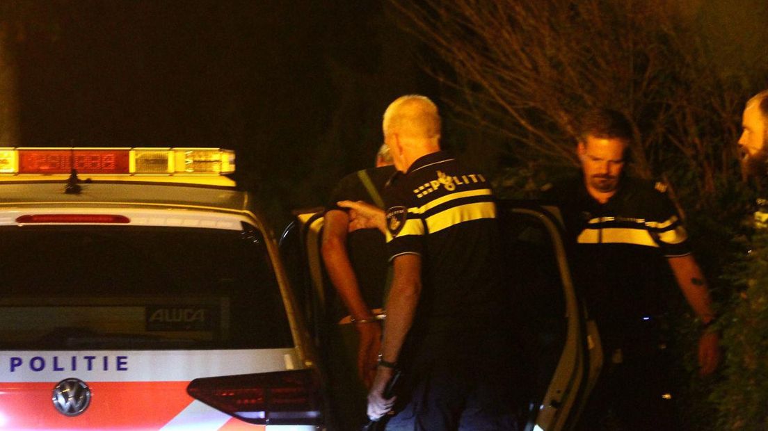 De verdachte wordt geboeid een politieauto ingeleid.