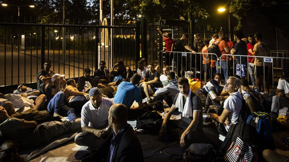 Asielzoekers wachten voor de poort op een opvangplek in Ter Apel