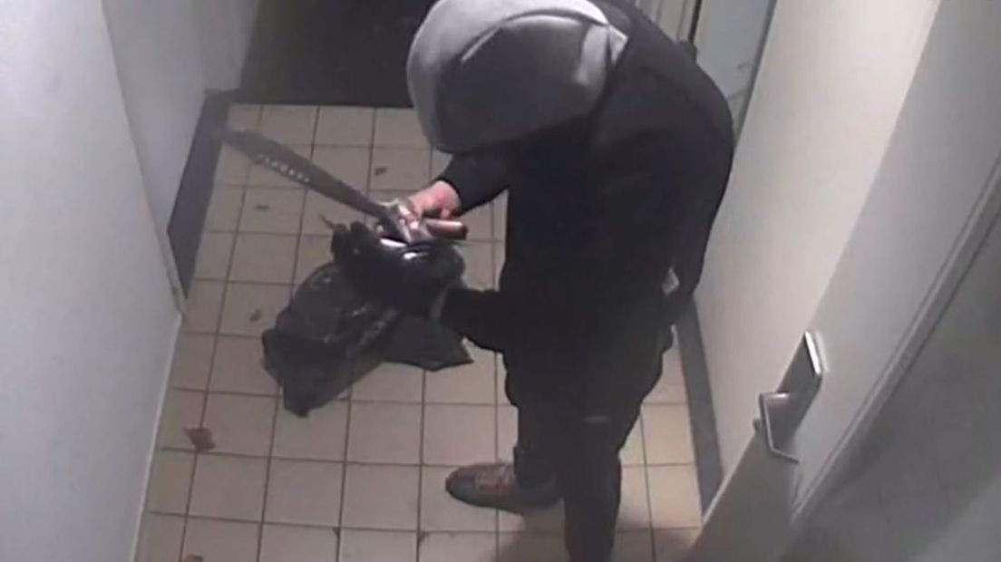 De overvaller, met machete, doorzoekt de portemonnee van de portier.