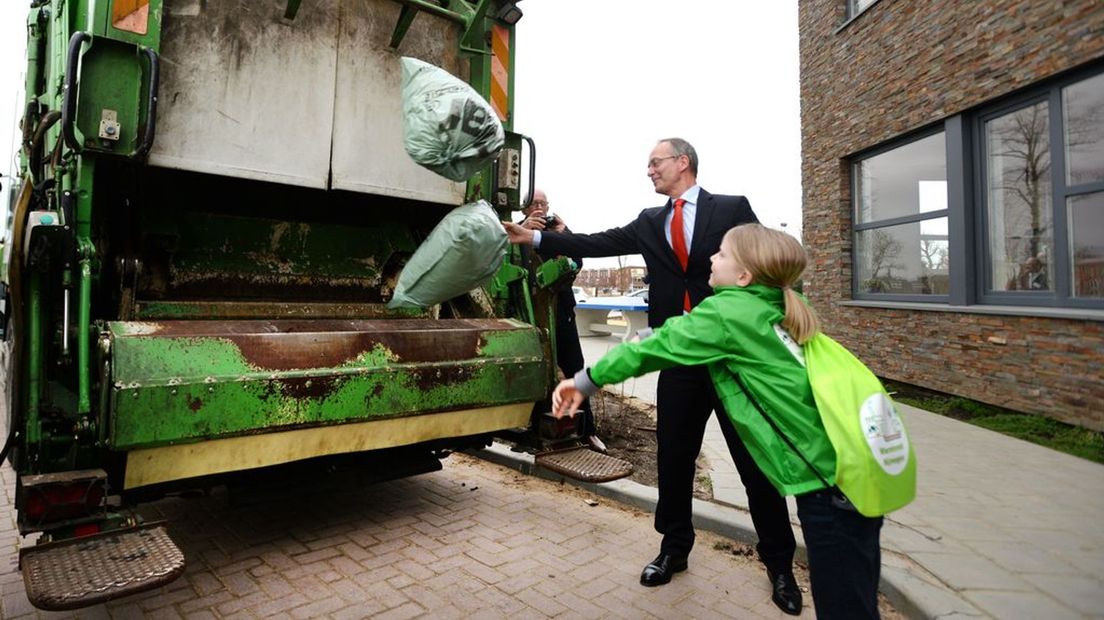 Toenmalige minister Henk Kamp van Economische Zaken gooit afvalzakken in een vuilnisauto tijdens de opening van het warmtenet in Nijmegen in 2015.