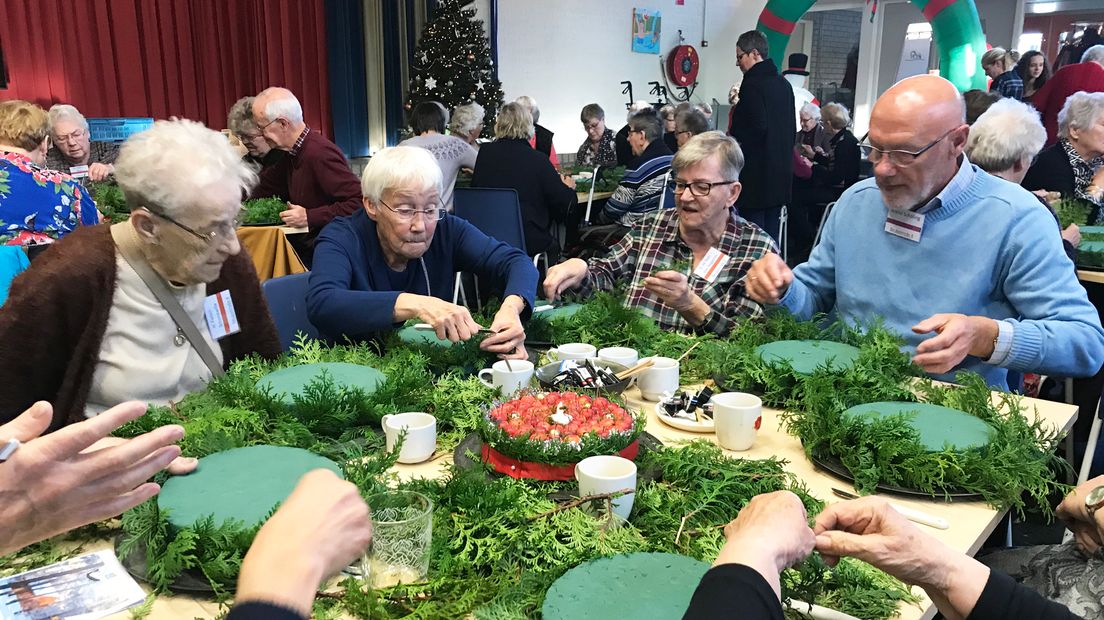 Ouderen zijn kerststukjes aan het maken in de grote Boszaal tijdens de midweek vakantie.