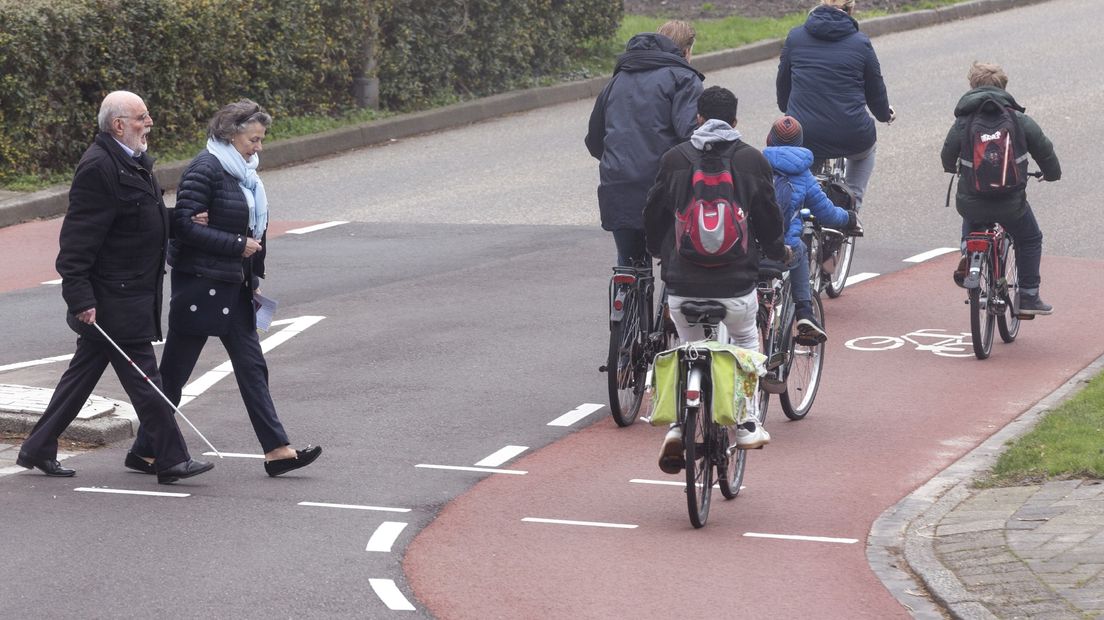 Een blinde man steekt onder begeleiding over