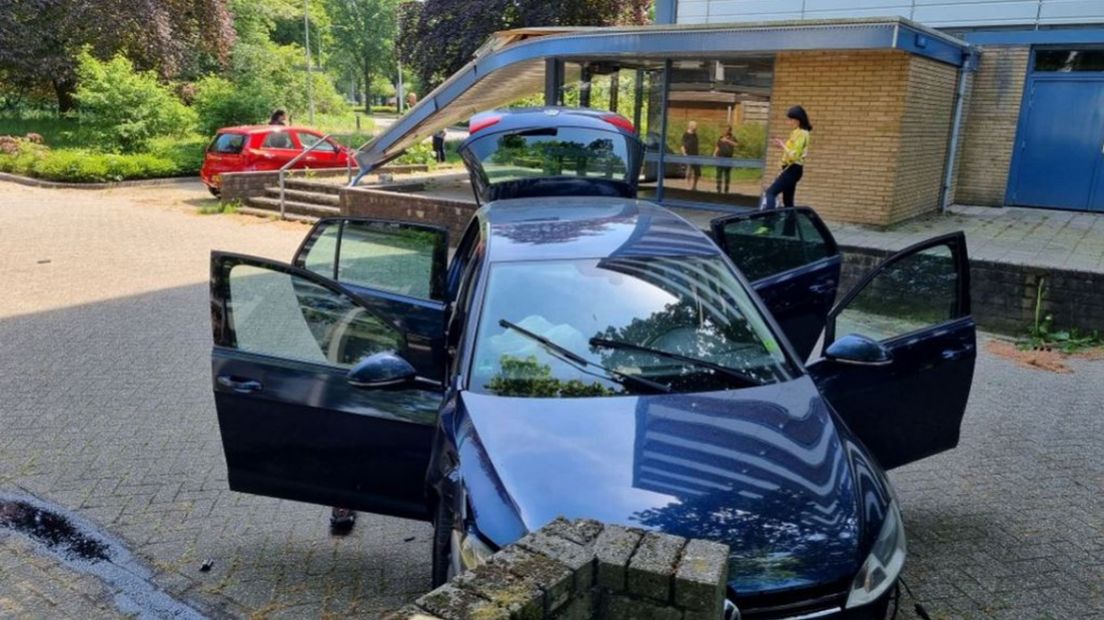 De auto met de beschadigde overkapping op de achtergrond.