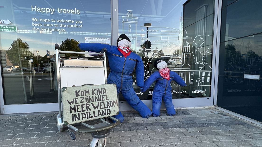 Stropoppen bij de luchthaven met de tekst: 'Kom kind, we zijn niet meer welkom in dit land'