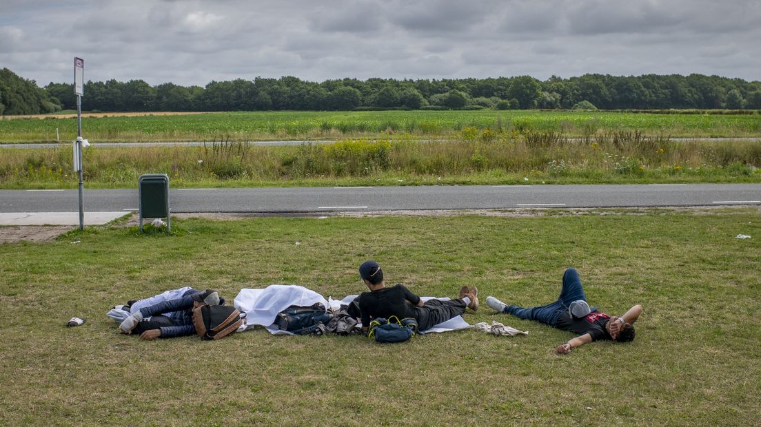 Asielzoekers liggen in het gras, bij het aanmeldcentrum in Ter Apel