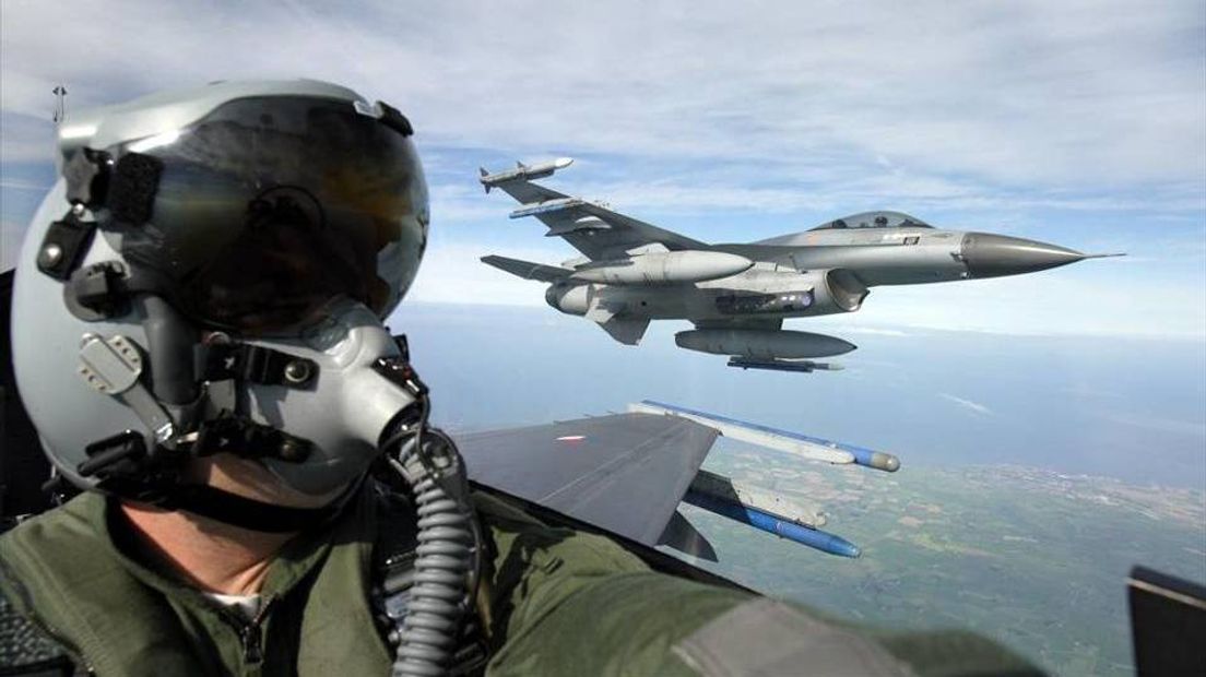 Een vlieger zit in de cockpit van een F-16 met op de achtergrond een tweede F-16 in de lucht