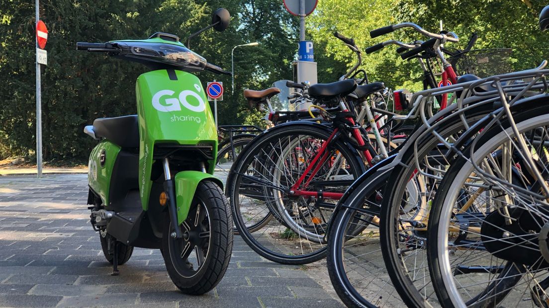 Een van de deelscooters geparkeerd achter fietsen in stad Groningen