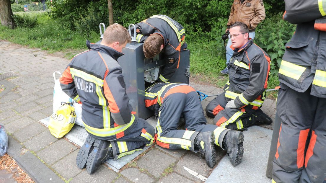 De brandweermannen reikte tot diep in de de vuilniscontainer met een afvalgrijper.