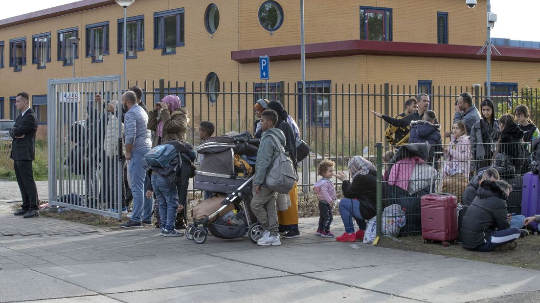 Asielzoekers, onder wie kinderen, wachten voor de poort van het azc in Ter Apel