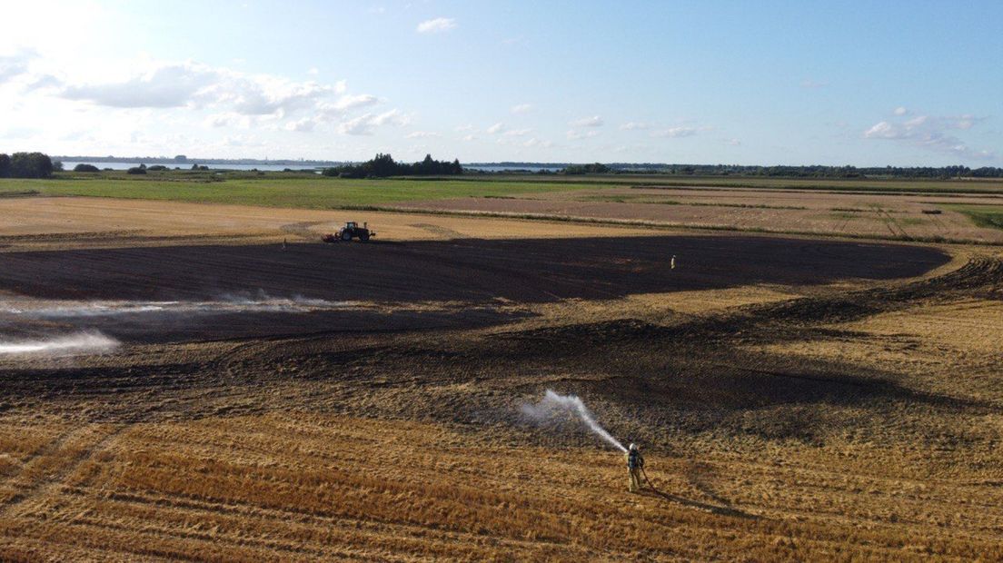 Een brandweerman is aan het nablussen, met op de achtergrond het Zuidlaardermeer