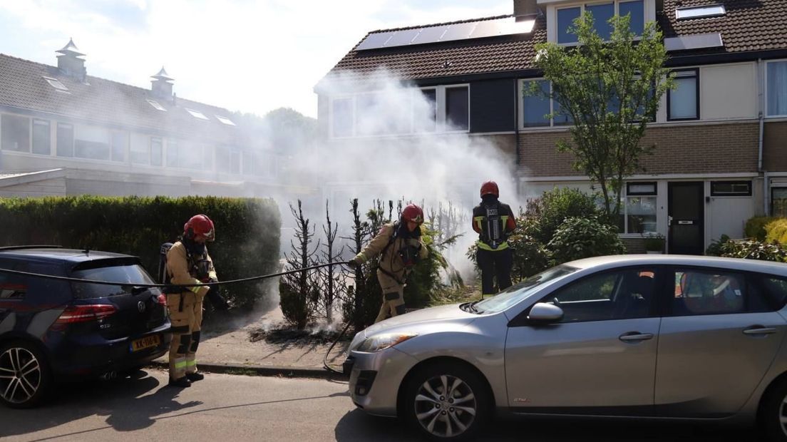 Brandweerlieden blussen de brand in de coniferenhaag