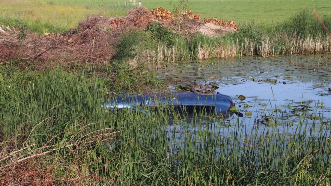 Auto op de kop in het water naast de dijk in Wilsum