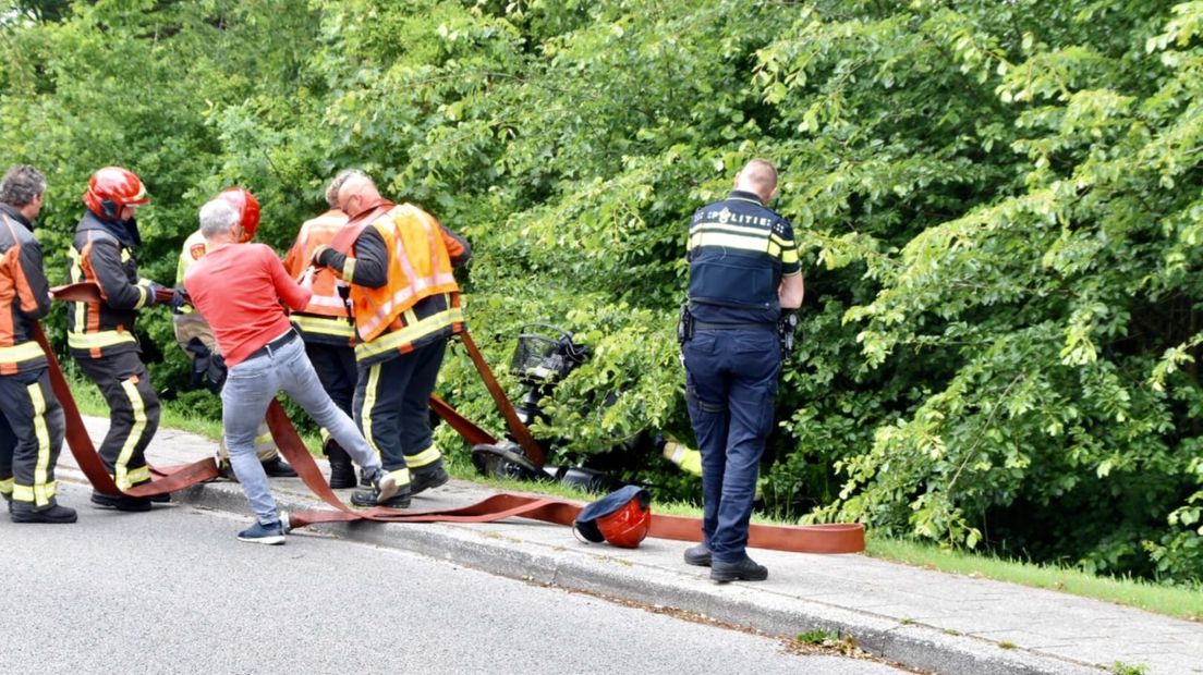 Een omstander en hulpdiensten trekken de scootmobiel uit de sloot