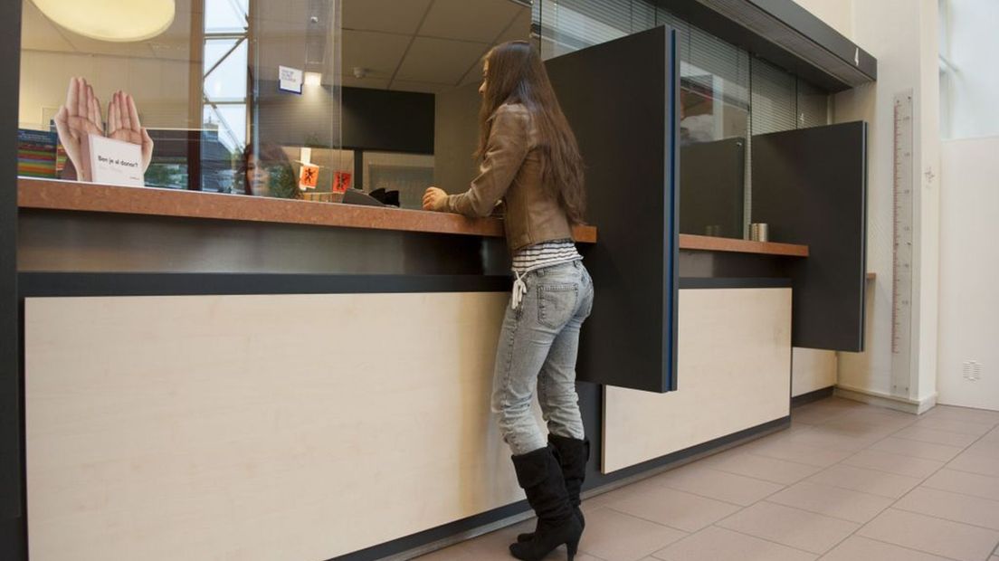 Iemand haalt een paspoort op bij de balie op het gemeentehuis.