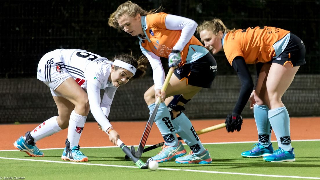 Laura van Weeren (GHHC) strijdt om de bal met Noor de Baat, met rechts Anouk van den Berg