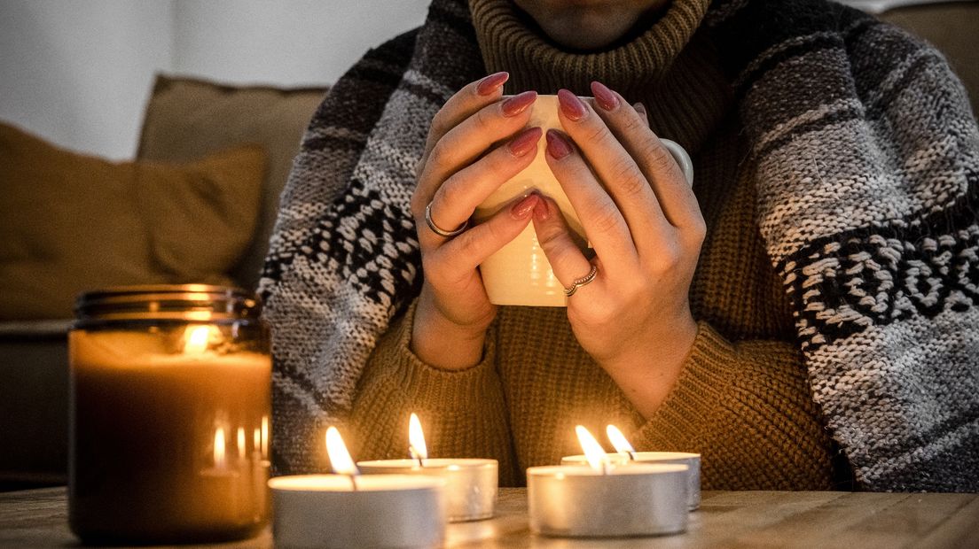 Een vrouw houdt zichzelf warm met een deken, warme thee en kaarsen