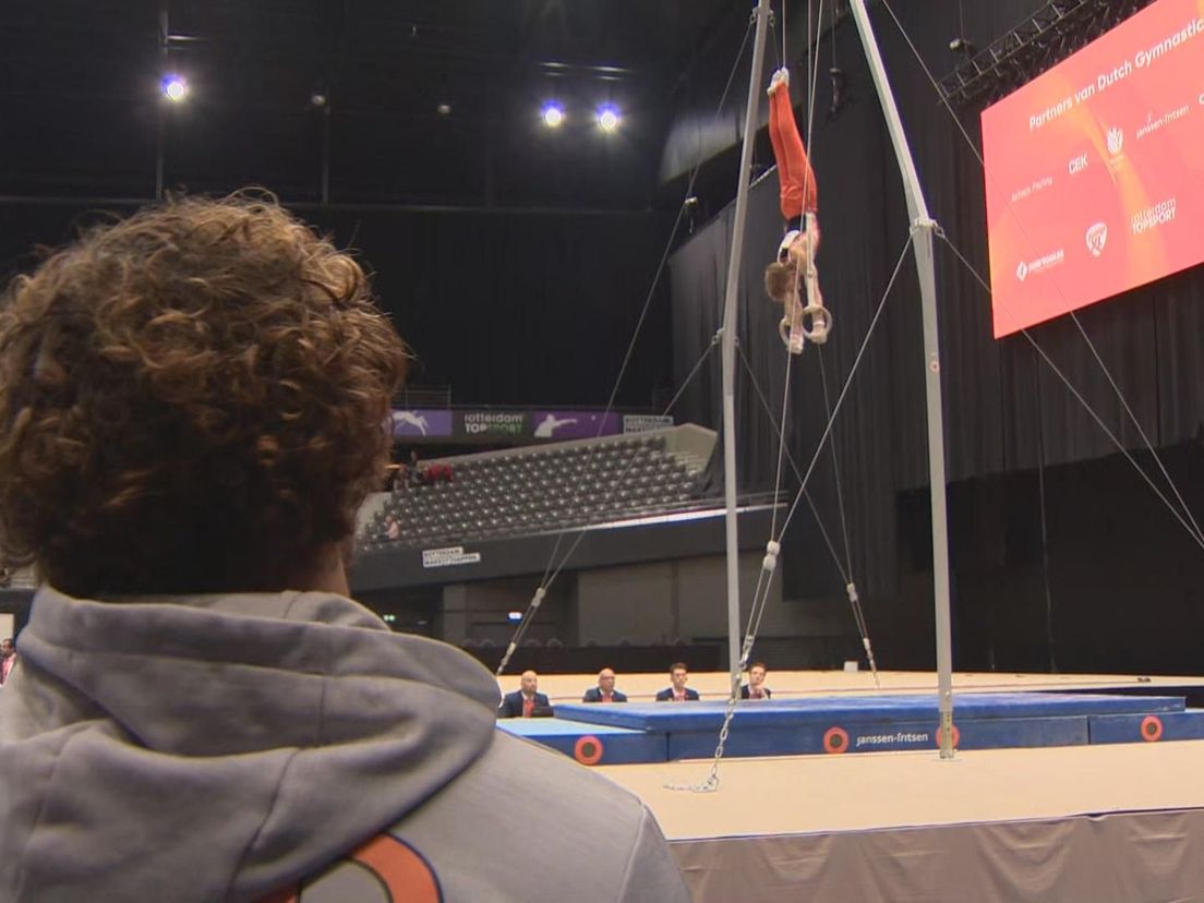 Bart Deurloo (met de rug naar de camera) staat te coachen op het NK Turnen