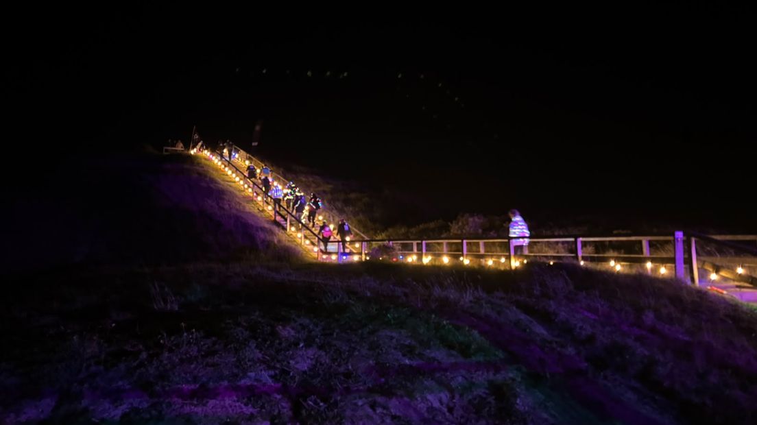 De lopers lopen via een verlichte trap bij het KNRM omhoog