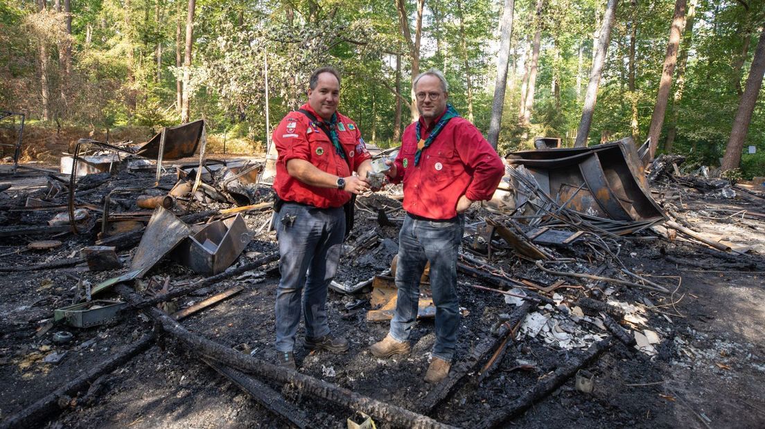 Bestuursleden Sander Koop en Gert Bos bij het afgebrande clubhuis. Beide scouts vonden tussen de brandresten een piepklein geldkistje. Het is nu het symbool van de crowdfundingactie.