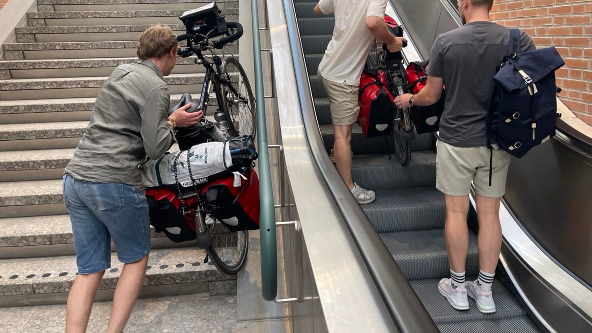 Twee mensen brengen hun fiets naar boven: de één met de roltrap, de ander met de gewone trap