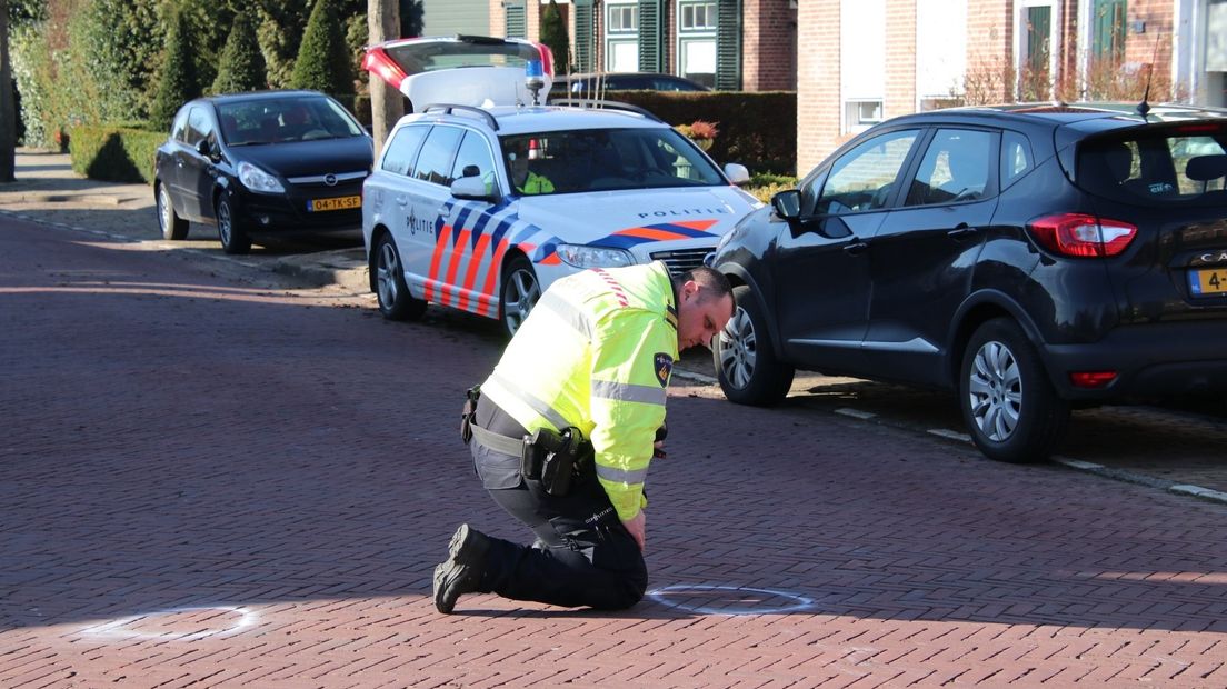 Een politieman onderzoekt de straat waar de fietser en auto in botsing kwamen