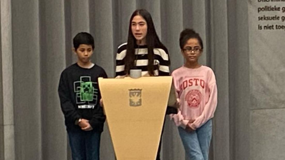 Asli spreekt met haar klasgenoten Elizabeth en Amaro de gemeenteraad toe.