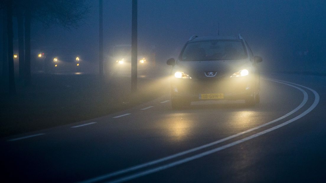 Een auto rijdt door de mist.