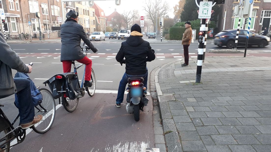 Een snorfiets wacht samen met fietsers voor een verkeerslicht in Stad