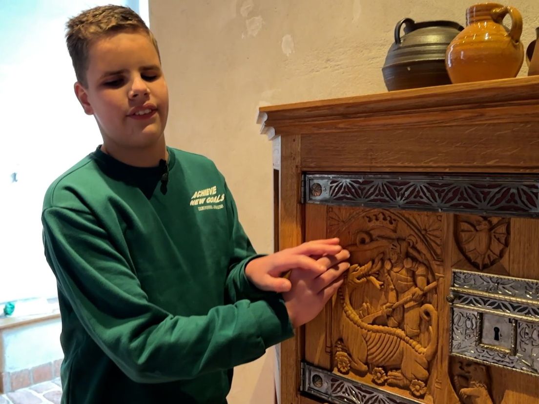 Mees van Helden voelt aan een afbeelding in houtsnijwerk op een kastdeurtje in een kasteel.