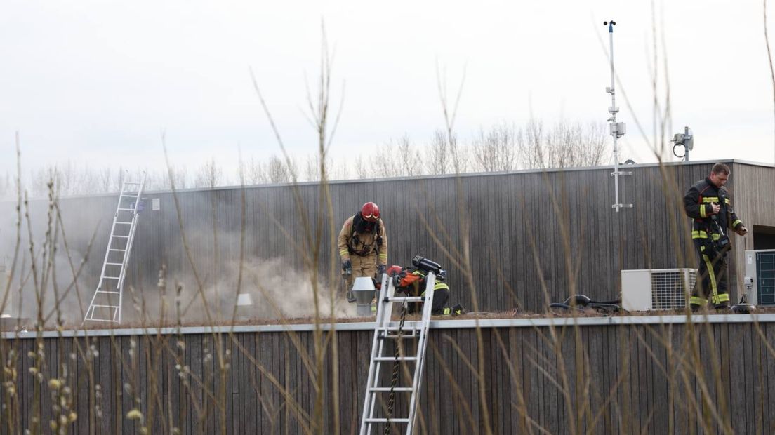Brandweermensen bij het rokende dak van het crematorium aan het Hoendiep in Groningen