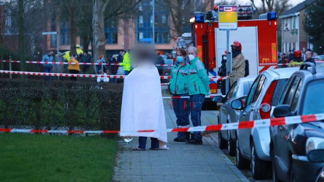 Een bewoner die uit het appartement is gehaald, volgt de reddingsactie op straat