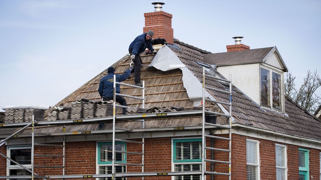 Bouwvakkers brengen een lichtgewicht schoorsteen aan op het dak van een huis in Zeerijp