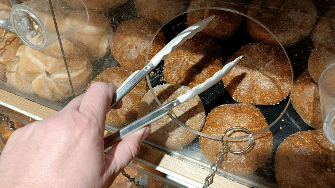 Een welopgevoed persoon gebruikt de tang om een broodje te pakken