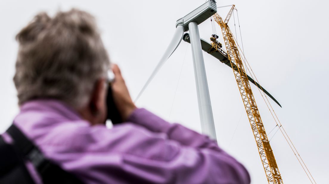 Een omstander kijkt hoe de wiek op een windmolen wordt geplaatst