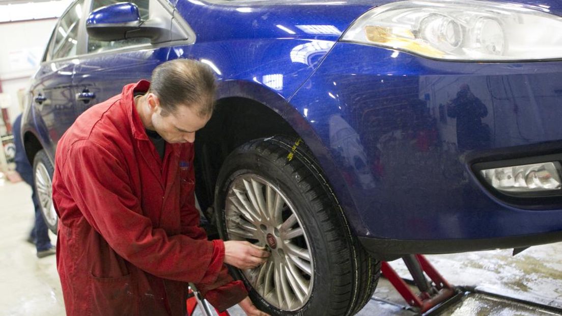 Een monteur zet winterbanden onder een auto.