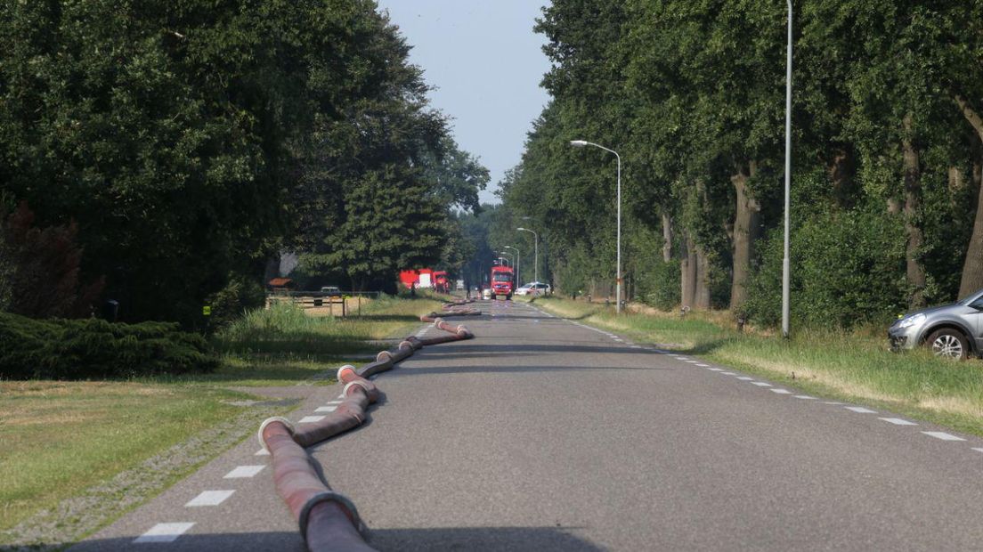 Met een lange slang wordt water naar de brand gepompt (Van Oost Media)